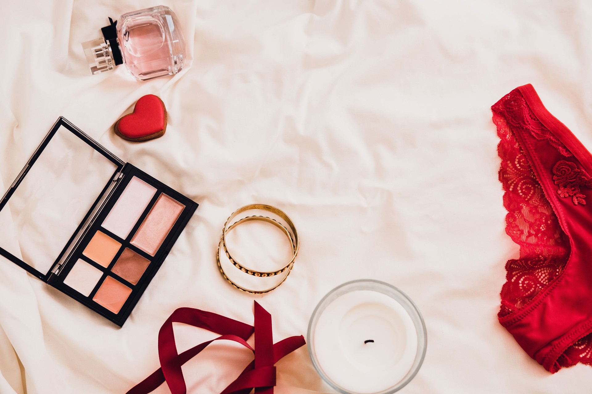 Woman's beauty products on white bed sheets flatlay